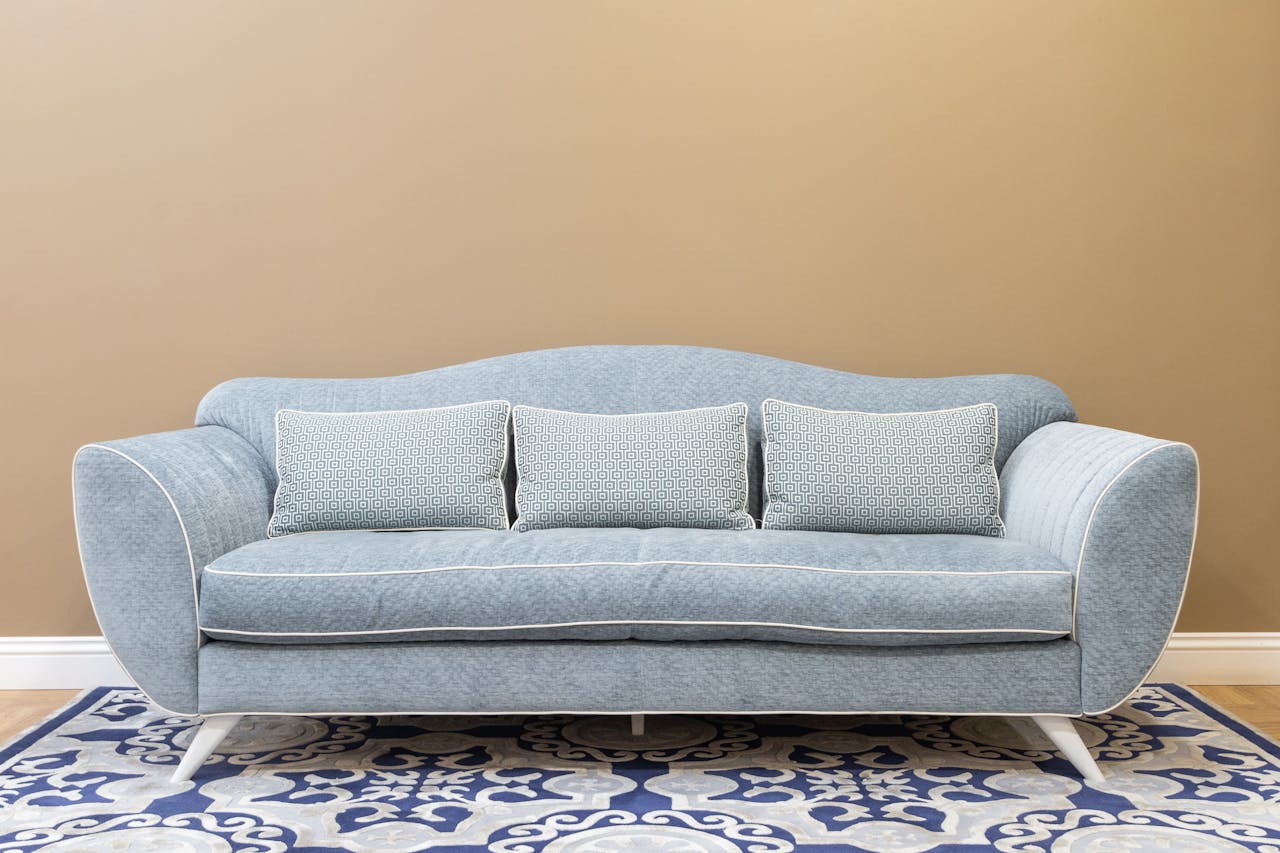 home-hero Stylish blue sofa with cushions on patterned carpet, perfect for a modern, cozy living space.